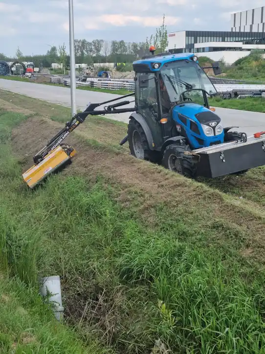 Tractor met maaiarm in actie op een berm