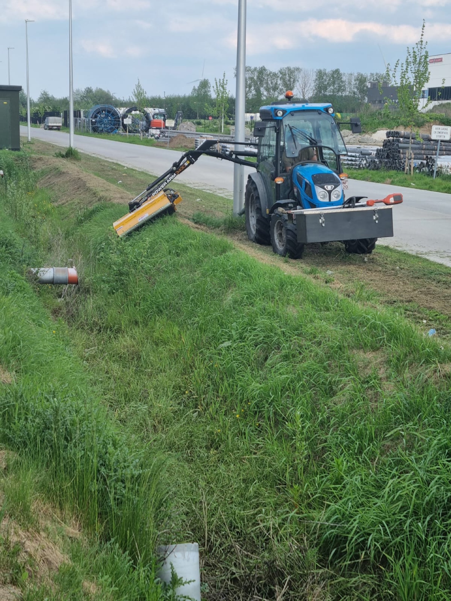 Tractor met maaiarm langs een baan op een industriezone